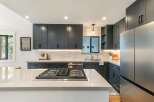 Experience modern luxury in this stunning kitchen, featuring sleek dark cabinetry, a spacious quartz island with a built-in gas range, and elegant subway tile backsplash.