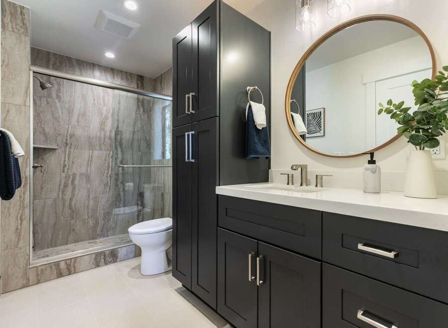 This modern bathroom features a sleek dark vanity with ample storage and a white quartz countertop.