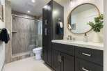 This modern bathroom features a sleek dark vanity with ample storage and a white quartz countertop.