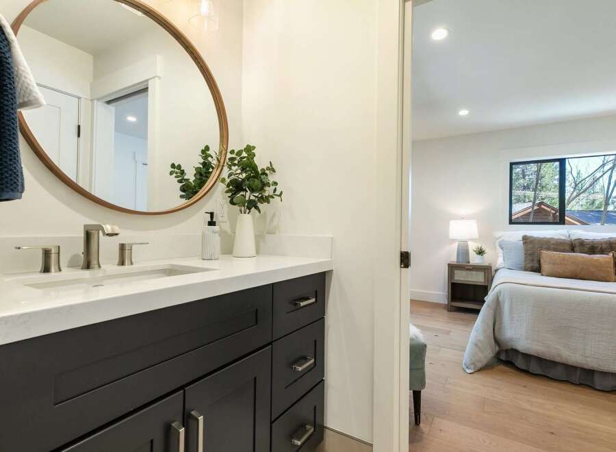 This modern bathroom features a sleek dark vanity with brushed nickel hardware and a white quartz countertop, complemented by a large oval mirror.