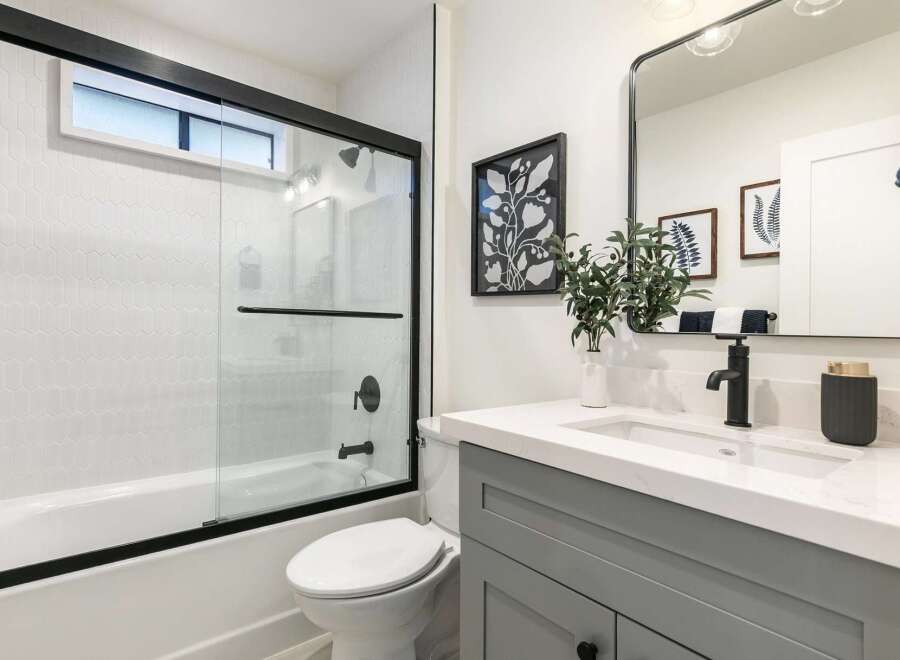 This modern bathroom features a sleek white bathtub with a glass shower door and white geometric tile.