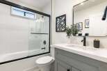 This modern bathroom features a sleek white bathtub with a glass shower door and white geometric tile.