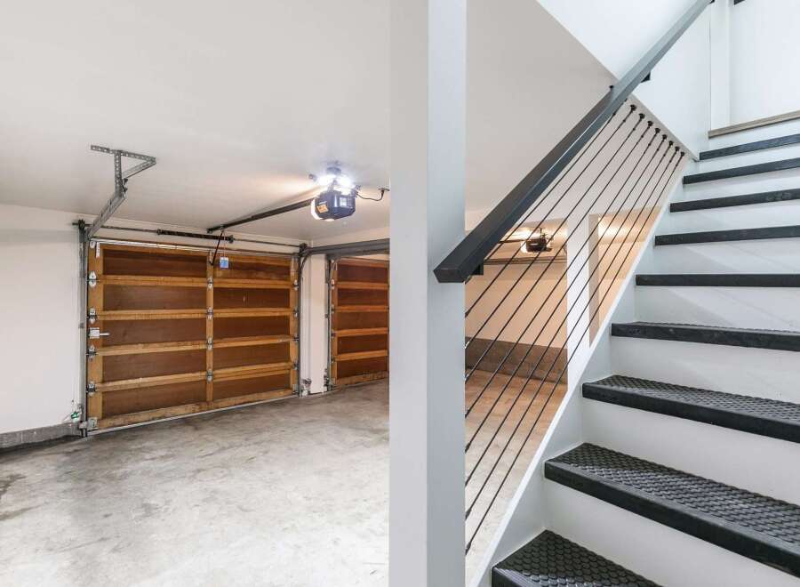 This image showcases a modern garage with two wooden garage doors and a sleek staircase with black cable railings.