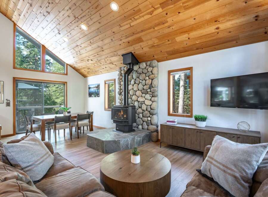 Experience cozy living in this charming cabin-style living room, featuring a striking stone fireplace with a wood-burning stove as the centerpiece.