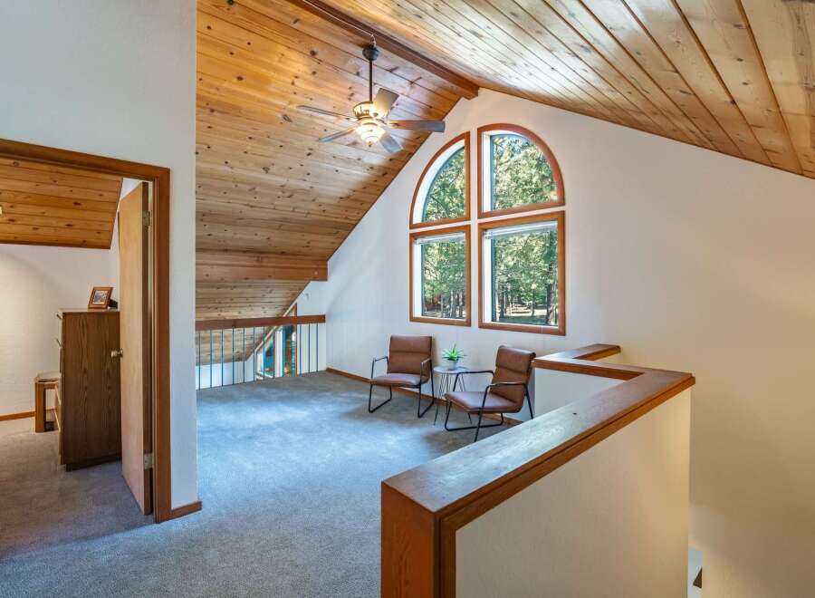 Ascend to this charming loft space, featuring a vaulted wood-paneled ceiling and a striking arched window that floods the area with natural light and offers serene forest views.