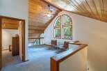 Ascend to this charming loft space, featuring a vaulted wood-paneled ceiling and a striking arched window that floods the area with natural light and offers serene forest views.