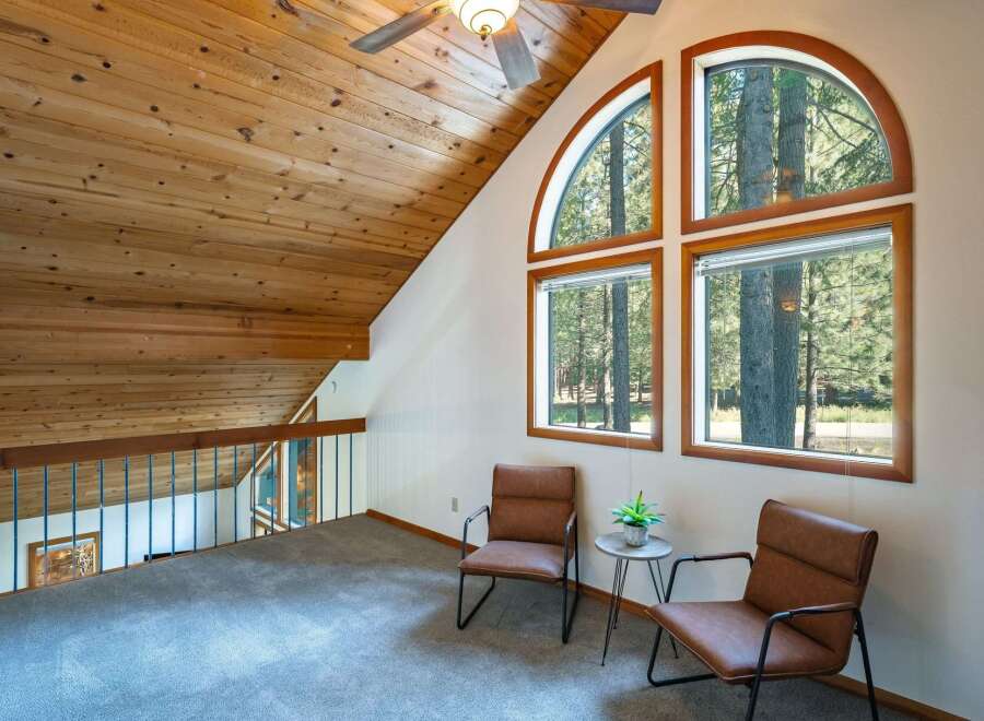 Ascend to this charming loft space, featuring a vaulted wood-paneled ceiling and a stunning arched window that frames picturesque forest views.