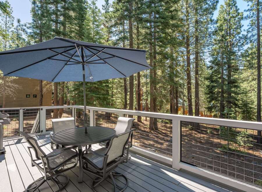 Enjoy outdoor dining and relaxation on this spacious deck, complete with a table, chairs, and a large umbrella for shade.