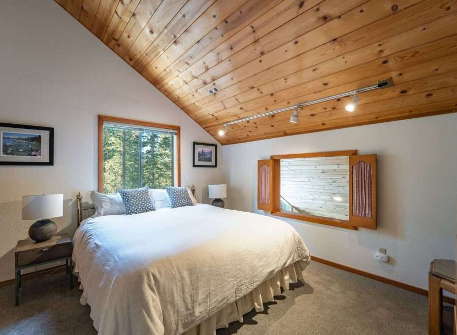Experience cozy mountain living in this charming bedroom, featuring a vaulted wood-paneled ceiling and a large window with serene forest views.