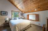 Experience cozy mountain living in this charming bedroom, featuring a vaulted wood-paneled ceiling and a large window with serene forest views.
