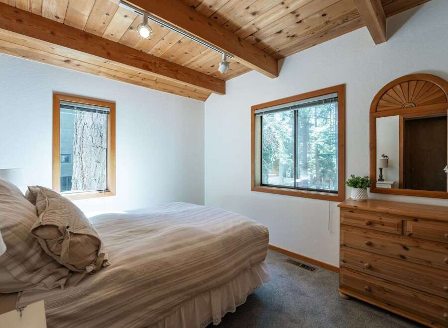 Experience cozy cabin living in this charming bedroom featuring a vaulted wood-beamed ceiling and ample natural light.