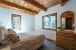 Experience cozy cabin living in this charming bedroom featuring a vaulted wood-beamed ceiling and ample natural light.