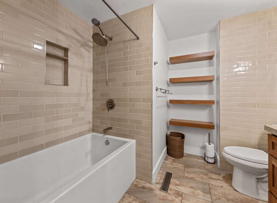 This modern bathroom features a sleek white bathtub with a built-in niche, complemented by elegant beige subway tile walls.