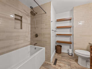 This modern bathroom features a sleek white bathtub with a built-in niche, complemented by elegant beige subway tile walls.