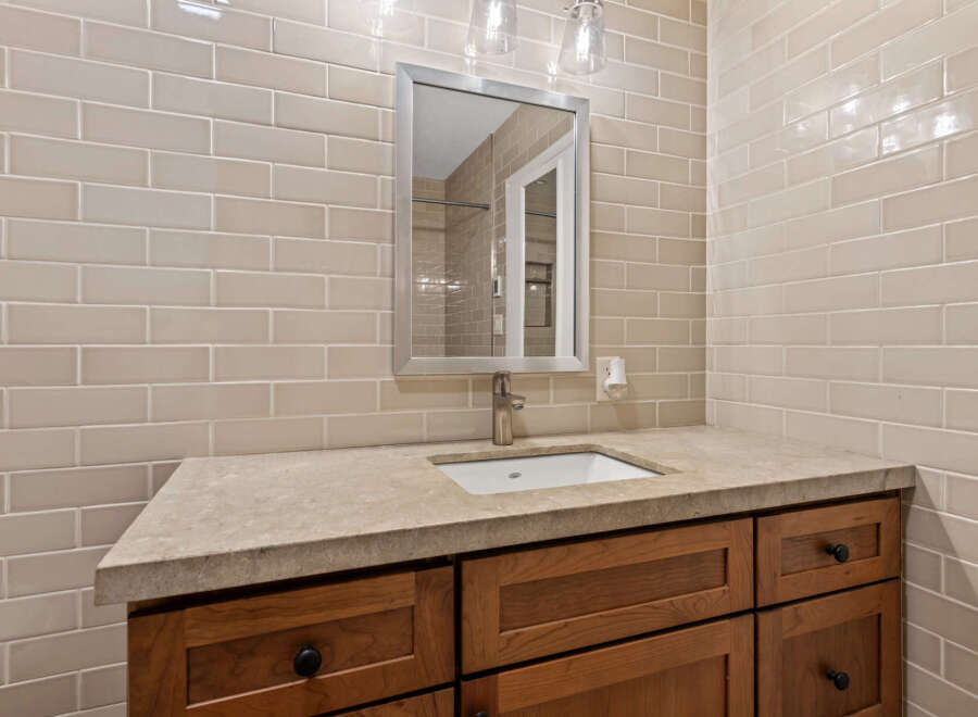 This bathroom vanity features a light beige subway tile backsplash that complements the natural stone countertop.