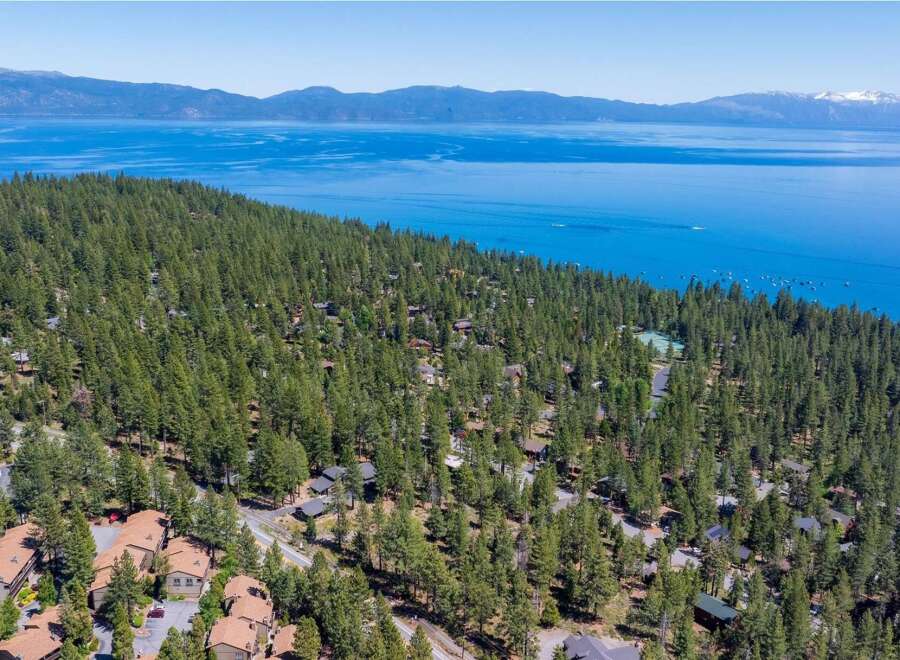 Nestled amidst a dense forest of tall pine trees, this property offers a serene retreat with stunning views of a vast, blue lake and distant mountains.