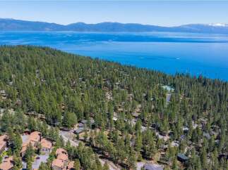 Nestled amidst a dense forest of tall pine trees, this property offers a serene retreat with stunning views of a vast, blue lake and distant mountains.