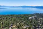Experience the ultimate lakeside living with this stunning aerial view of homes nestled among tall pine trees, offering breathtaking vistas of a vast, blue lake and distant snow-capped mountains.