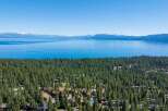 Experience the ultimate lakeside living with this stunning aerial view of homes nestled amidst a dense pine forest, offering breathtaking vistas of a vast, shimmering lake and distant snow-capped mountains.