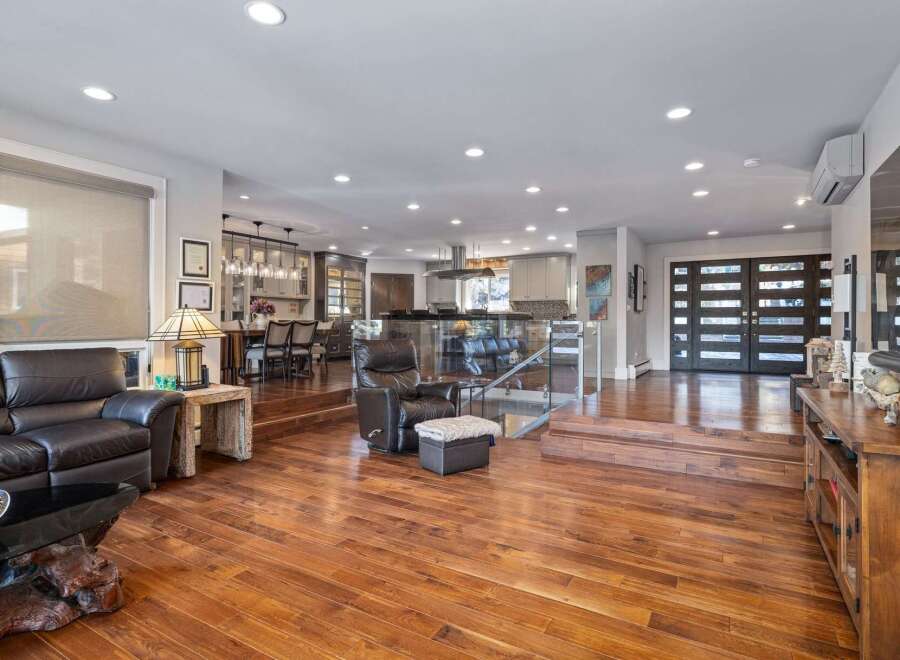 Experience luxurious open-concept living in this stunning home, featuring a spacious living area with a plush leather sofa and a modern glass-railed staircase leading to a gourmet kitchen and dining space.