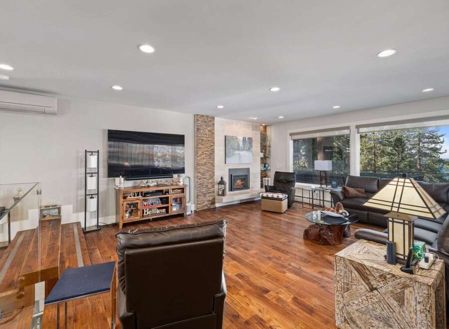 Experience breathtaking mountain and lake views from this stunning living room, featuring a modern fireplace and expansive windows.