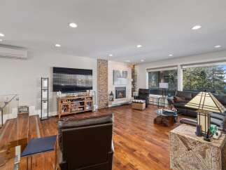 Experience breathtaking mountain and lake views from this stunning living room, featuring a modern fireplace and expansive windows.