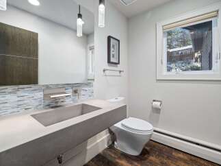 This modern bathroom features a sleek concrete sink and vanity, complemented by a striking mosaic tile backsplash.