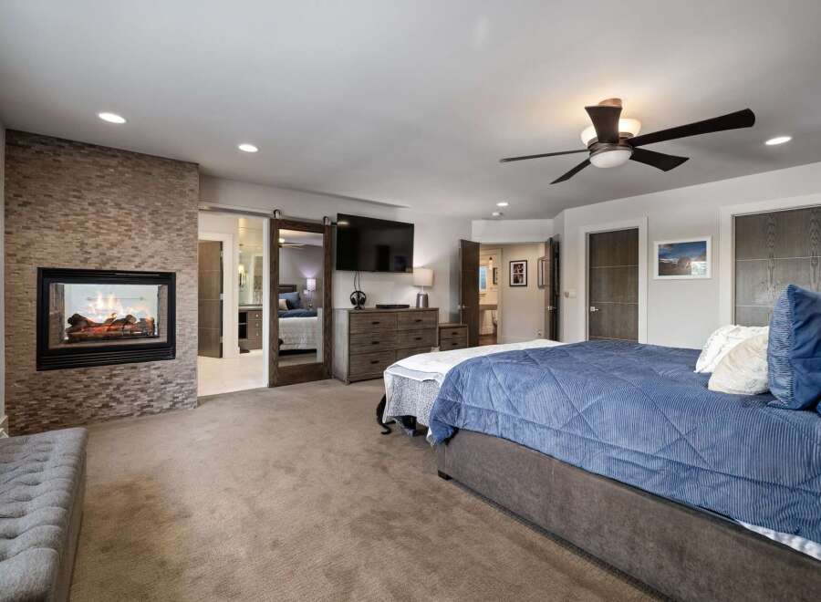 Experience luxury and comfort in this master suite, featuring a modern gas fireplace with a stacked stone surround and a large flat-screen TV.