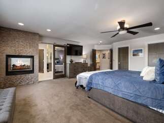 Experience luxury and comfort in this master suite, featuring a modern gas fireplace with a stacked stone surround and a large flat-screen TV.