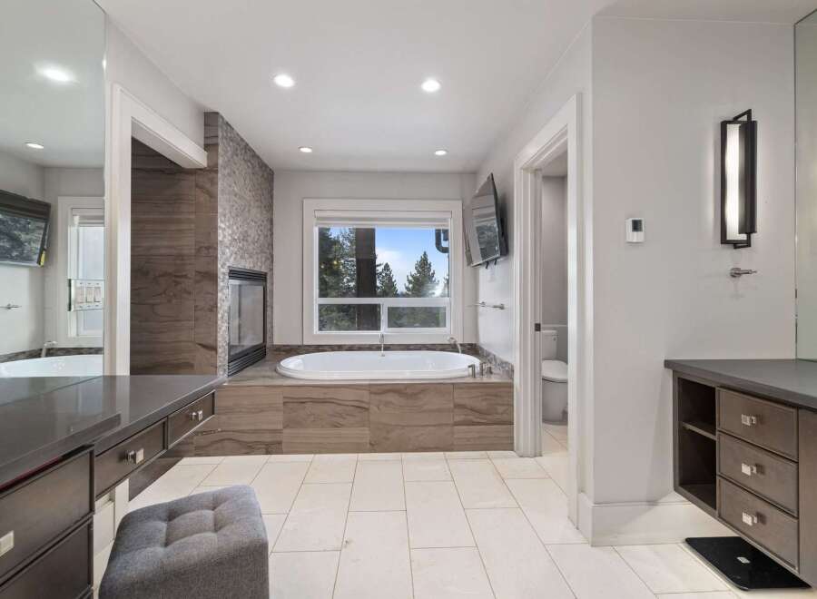 Indulge in luxury in this stunning master bathroom, featuring a deep soaking tub with a picturesque view of the surrounding trees.