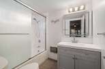 This modern bathroom features a sleek gray vanity with a white countertop and a large, illuminated mirror.