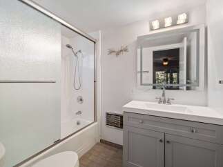This modern bathroom features a sleek gray vanity with a white countertop and a large, illuminated mirror.