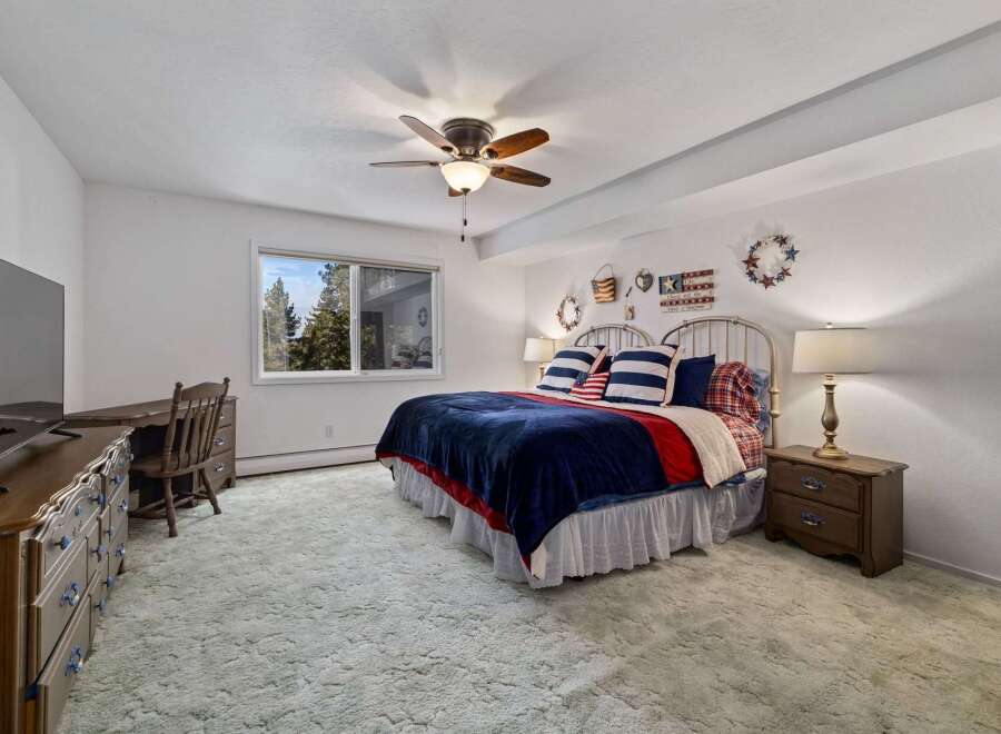 This charming bedroom features a comfortable queen-size bed adorned with patriotic-themed bedding, including striped pillows and a navy blue plush throw.