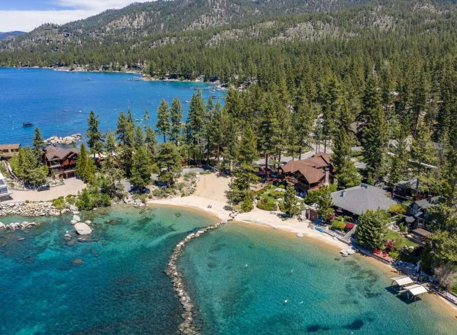 Experience luxury lakeside living with this stunning property featuring a private sandy beach and crystal-clear turquoise waters.