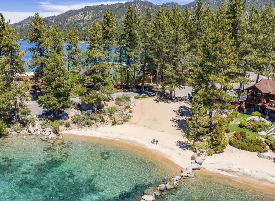 Experience luxury lakeside living with this stunning property featuring a private sandy beach and crystal-clear turquoise waters.