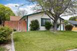 Charming single-story home featuring a welcoming front yard with lush green grass and mature trees.