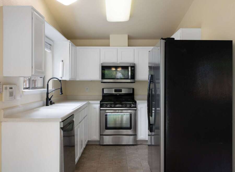 Discover this charming kitchen featuring sleek white cabinetry and modern stainless steel appliances, including a microwave and a gas range.