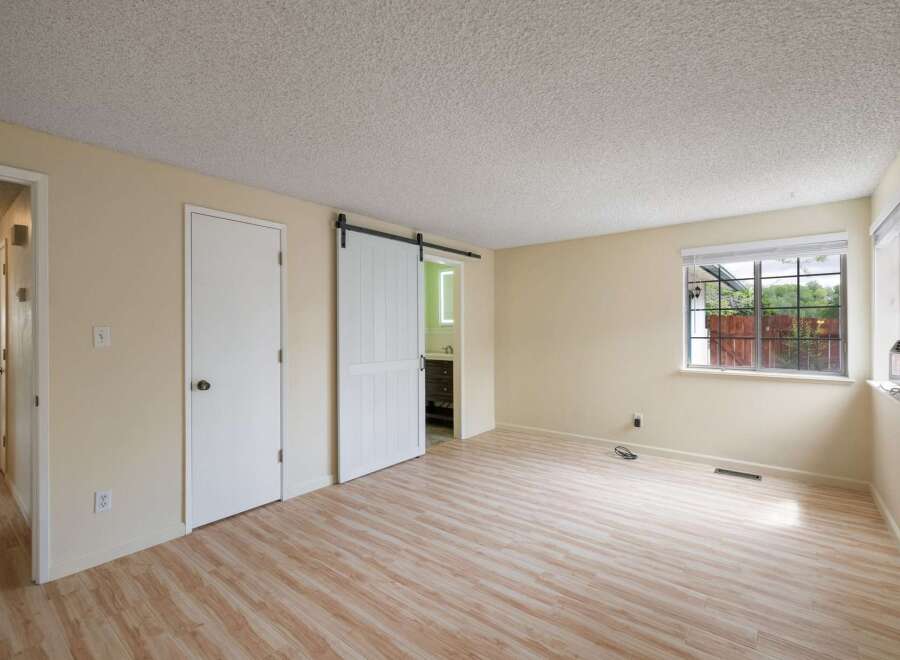 Discover this spacious room featuring a modern white sliding barn door leading to a bathroom.