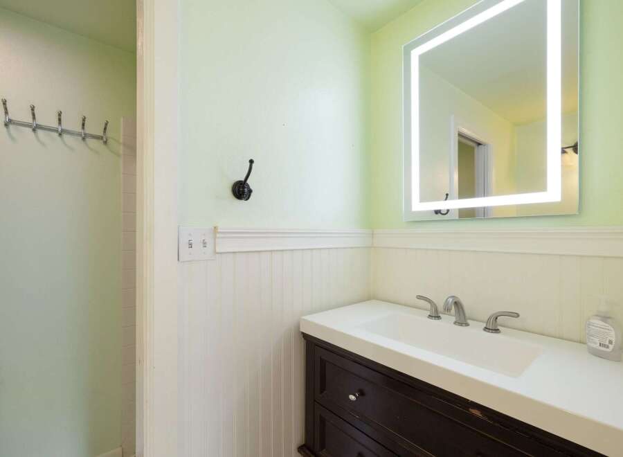 This bathroom features a modern vanity with a sleek white countertop and dark wood cabinetry, complemented by a large, illuminated mirror.