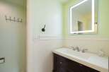 This bathroom features a modern vanity with a sleek white countertop and dark wood cabinetry, complemented by a large, illuminated mirror.