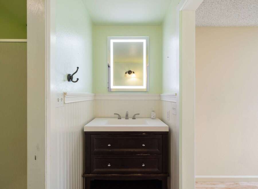 This bathroom features a modern vanity with a sleek white countertop and a dark wood cabinet, complemented by a bright LED-lit mirror.