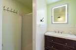 This bathroom features a modern vanity with a sleek white countertop and dark wood drawers, complemented by a large, illuminated mirror.