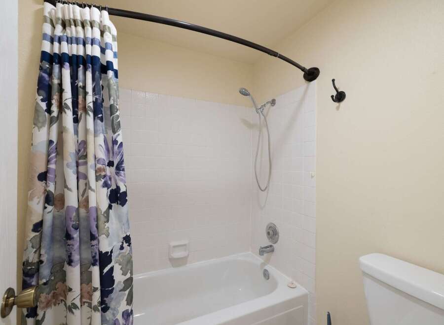 This bathroom features a clean white bathtub with a floral shower curtain and a handheld showerhead.