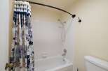 This bathroom features a clean white bathtub with a floral shower curtain and a handheld showerhead.