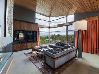 Experience breathtaking panoramic views from this stunning living room, featuring expansive floor-to-ceiling windows that frame a lush forest landscape.