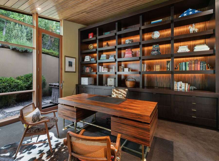 This luxurious home office features a stunning custom-built dark wood bookshelf with integrated lighting, showcasing a curated collection of books and decorative items.