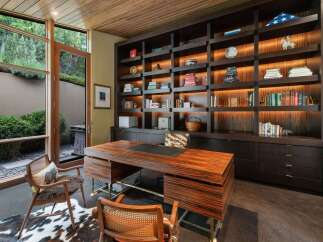 This luxurious home office features a stunning custom-built dark wood bookshelf with integrated lighting, showcasing a curated collection of books and decorative items.