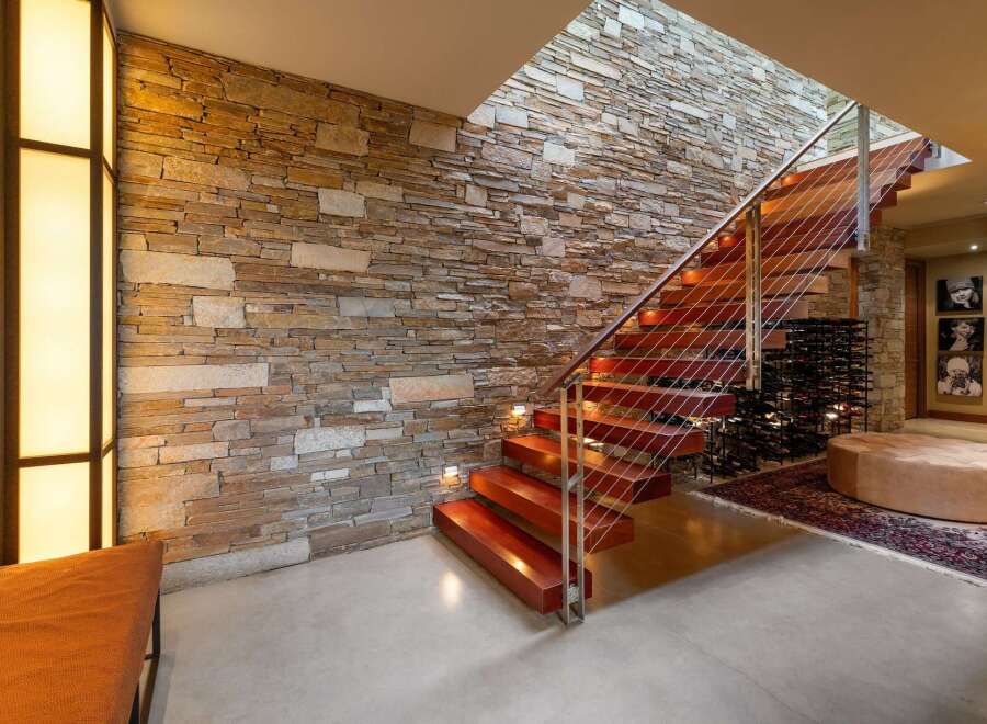 Experience modern luxury with this stunning staircase featuring rich wood treads and a sleek cable railing system, set against a dramatic stacked stone accent wall.
