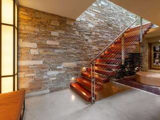 Experience modern luxury with this stunning staircase featuring rich wood treads and a sleek cable railing system, set against a dramatic stacked stone accent wall.