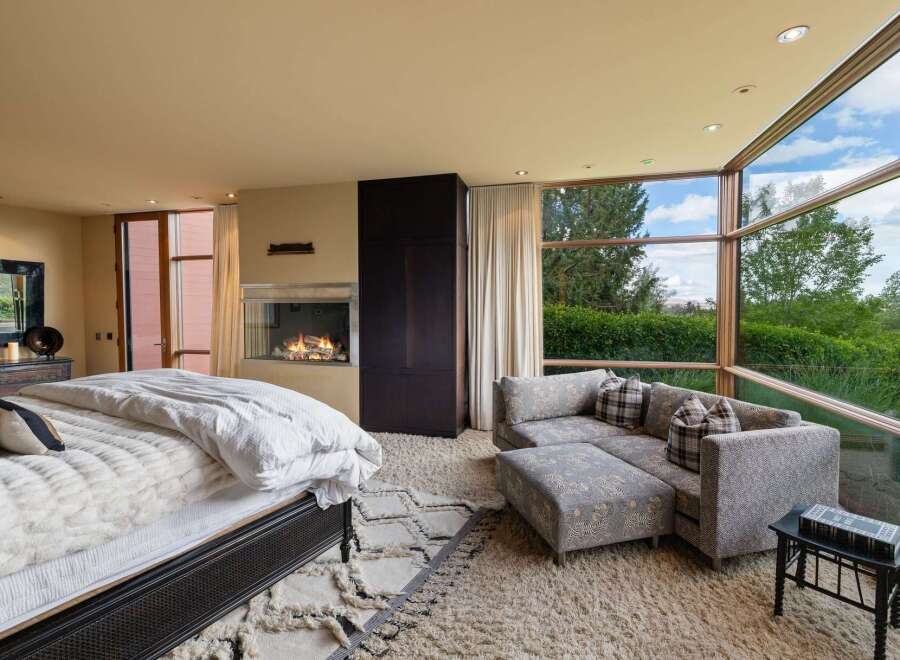 Experience luxury living in this master suite featuring a modern gas fireplace and expansive floor-to-ceiling windows that offer breathtaking views of the surrounding greenery.